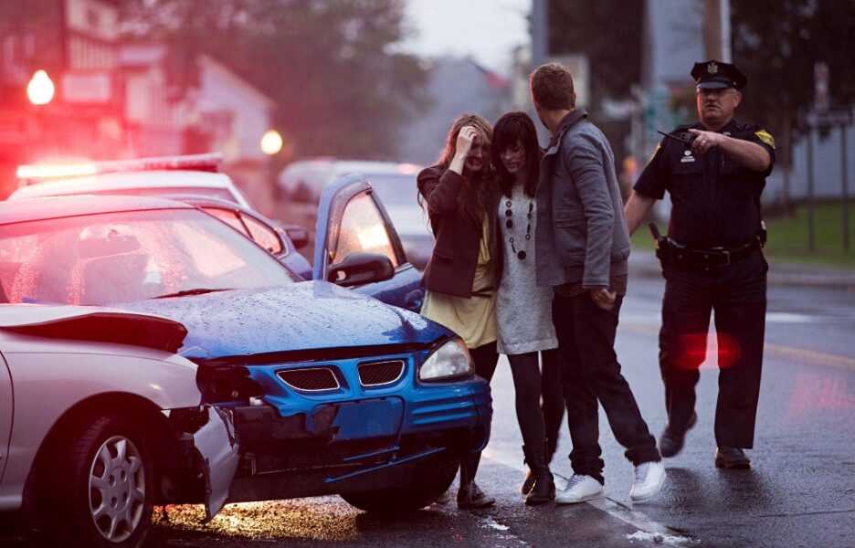 Police officer directs traffic as a man comforts a woman beside a car accident scene