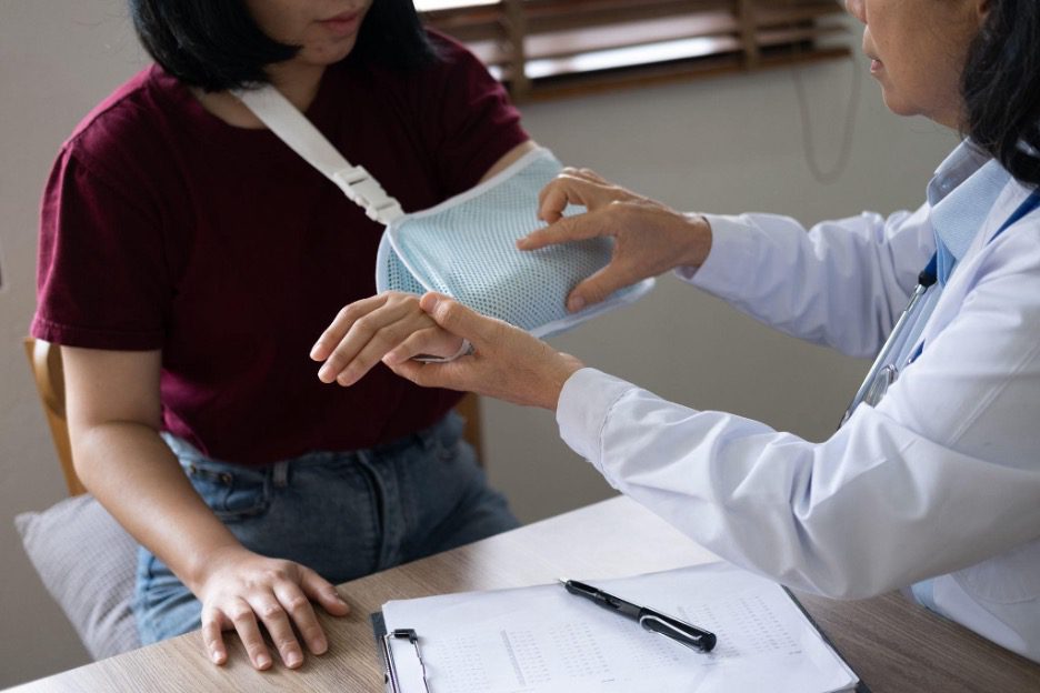 Patient wearing an arm sling speaks with an orthopedic doctor during a medical evaluation.