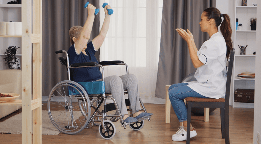 Physiotherapist assisting a wheelchair user with a light strength exercise during rehabilitation.